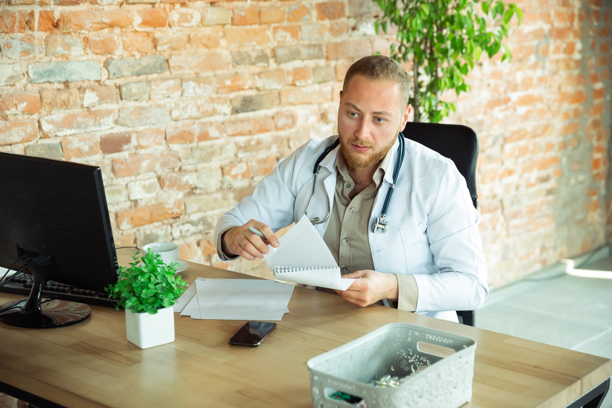 A Caucasian doctor consulting a patient, explaining a prescription in a medical office with cabinets in the background.